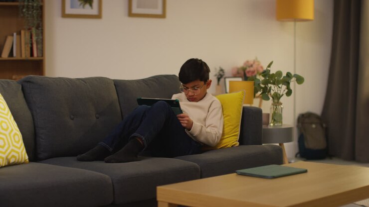 Ragazzino seduto sul divano a casa che gioca o guarda contenuti in streaming su un tablet digitale 4