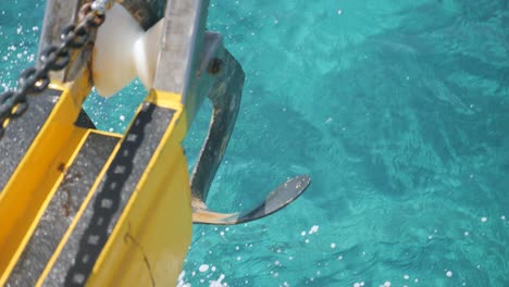 Close-up-of-a-boat-anchor-swaying-in-the-air-above-the-waters-as-waves-splash-up-against-it-in-slow-motion