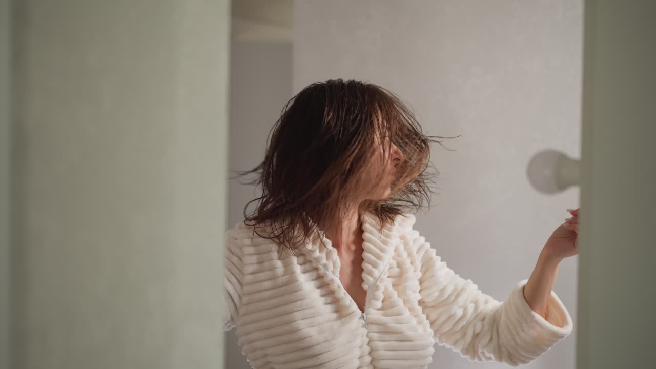 화장실에서 음악을 듣고 있는 여성, 어두운 머리카락을 가진 갈색 여성, 현대적인 화장실의 느린 동작에서 즐거운 음악을 듣는 여성.