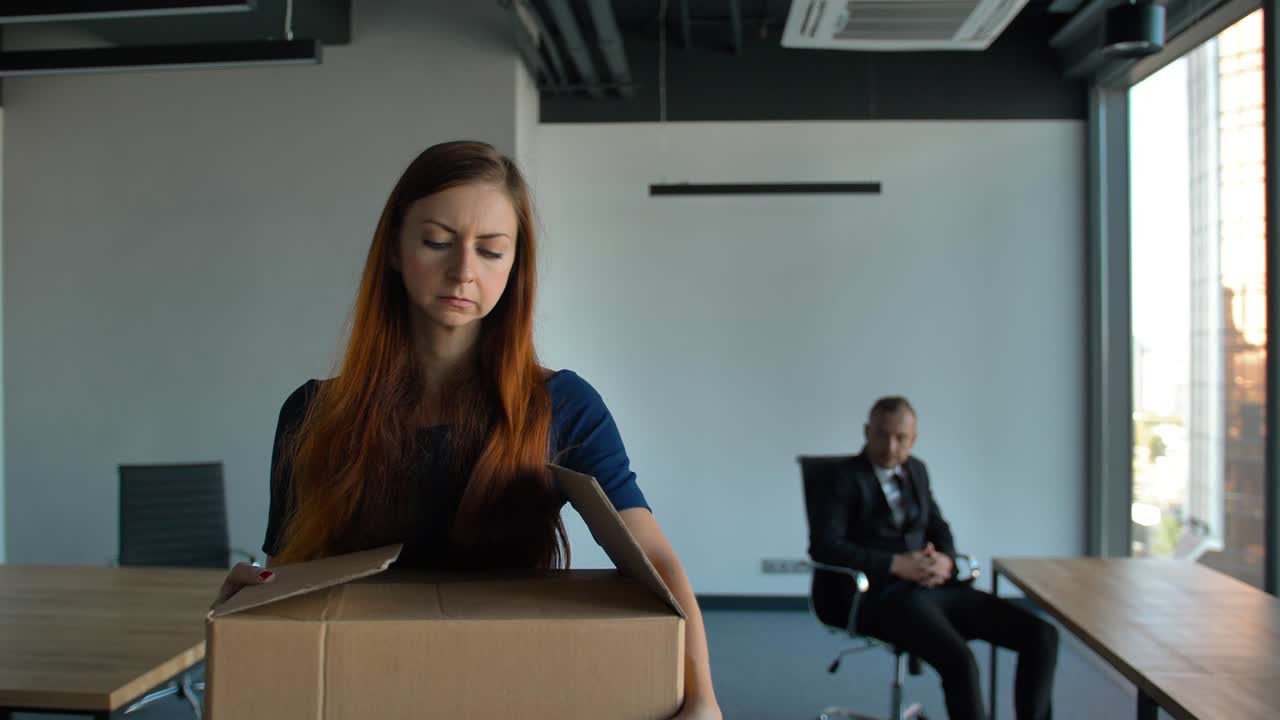 Sad employee packing her belongings and leaving the office after being fired