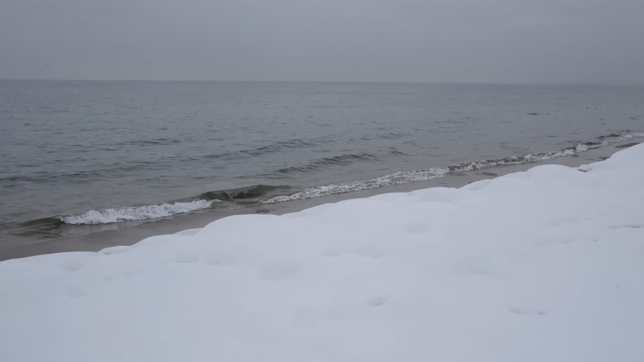 A serene video of a snowy beach with gentle waves, captured from a low-angle perspective