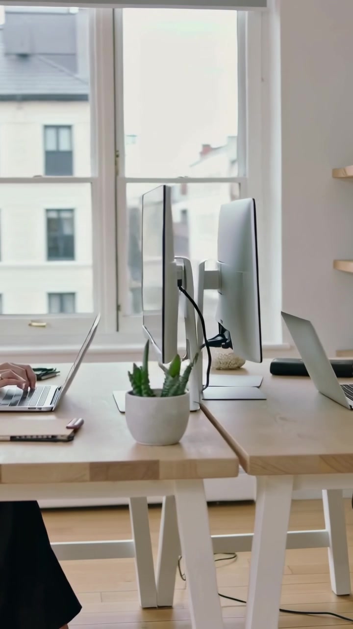 Video verticale: Panoramica a sinistra su un lavoratore che digita al laptop per lavoro alla scrivania, con maglione chiaro e monitor.