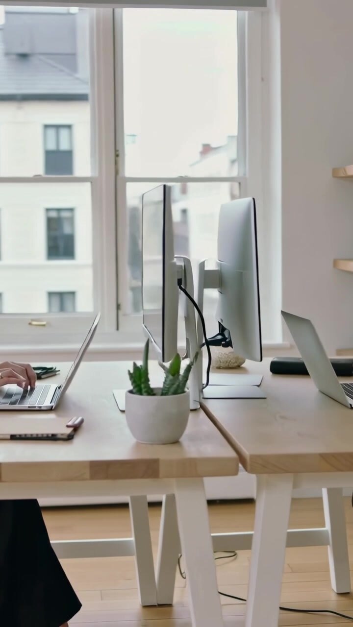 Video verticale: Panoramica a sinistra su un lavoratore che digita al laptop per lavoro alla scrivania, con maglione chiaro e monitor.