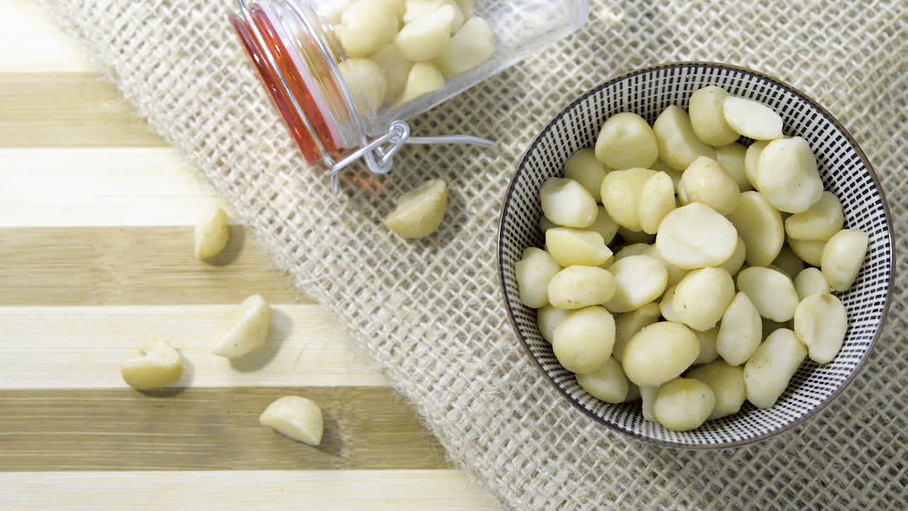 헤시안 천으로 줄무늬 테이블에 건포도 밤나무 혼합물로 채워진 유리병 세라믹 그릇을 통해 천천히 패닝 샷 위에서 아래로 보기