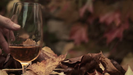 la mano pone suavemente un vaso de cerveza en la mesa de hojas en la escena de otoño, primer plano
