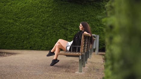 unique instagram dancer influencer revealing shot sitting on bench raising her leg stretching waiting for her date alone in green maze sad dissapointed impatient cloudy slow motion concrete ground