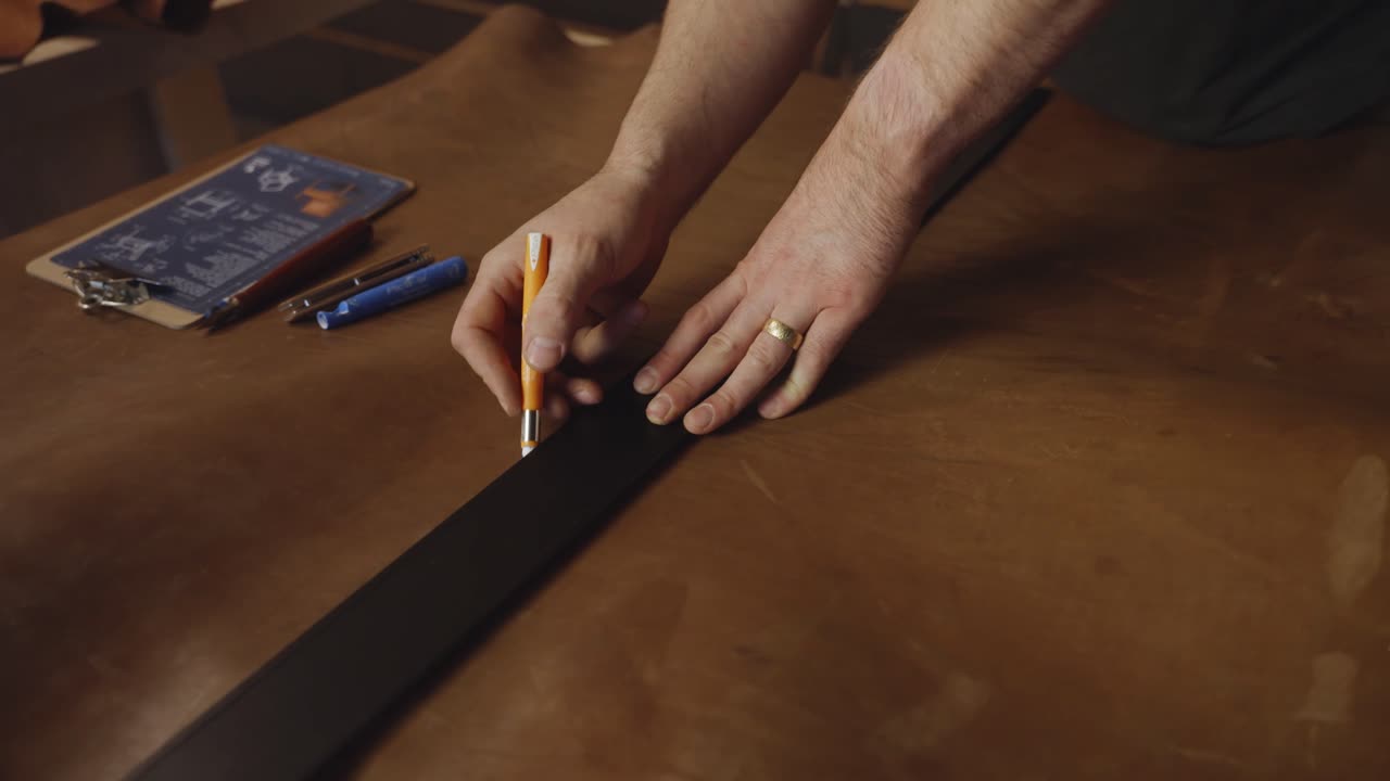 Close-up of an artisan carefully marking measurements on leather with a pencil and ruler in a workshop, showing precision, craftsmanship, and handmade design preparation