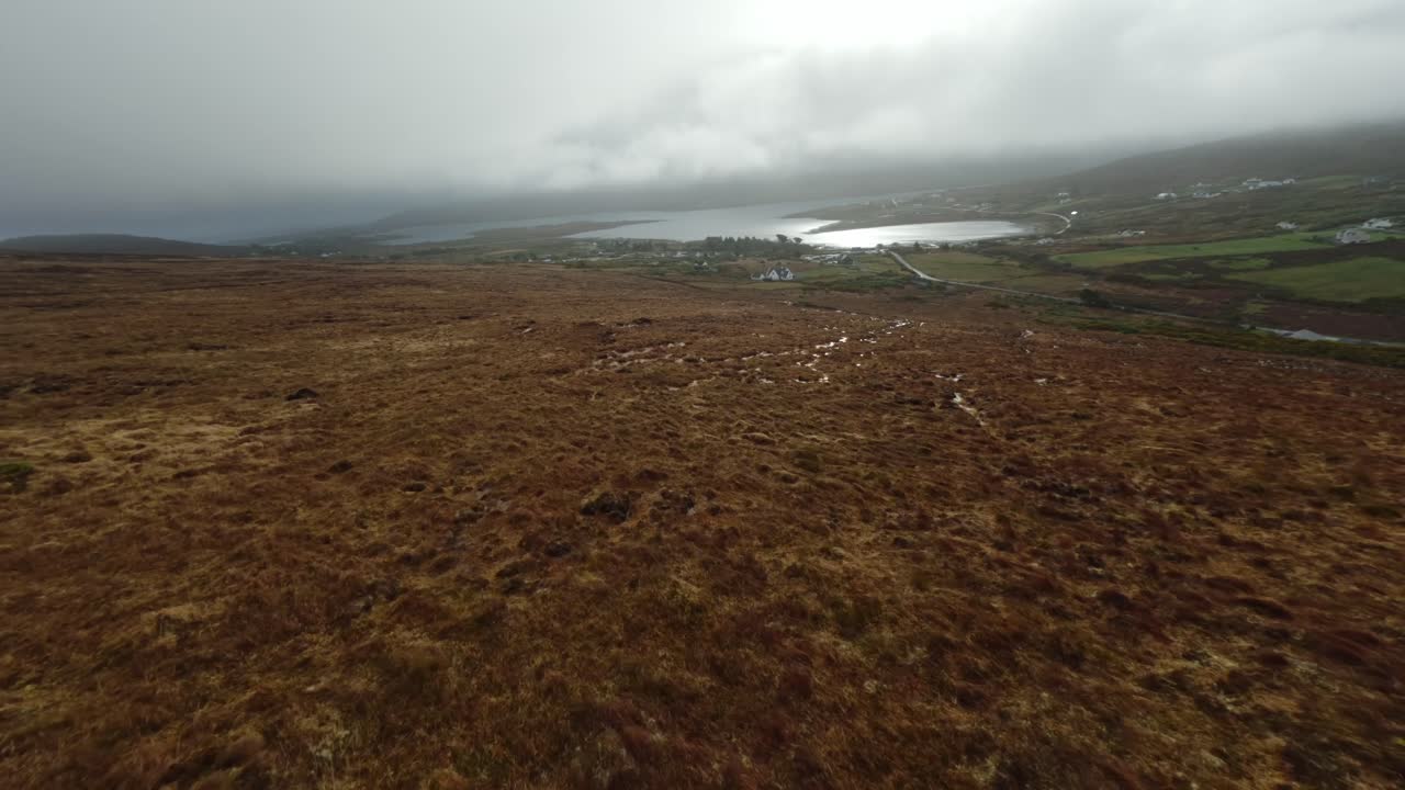 fpv 드론이 아일랜드의 바다 근처의 마을을 향해 언덕을 따라 빠르게 날고 있습니다.