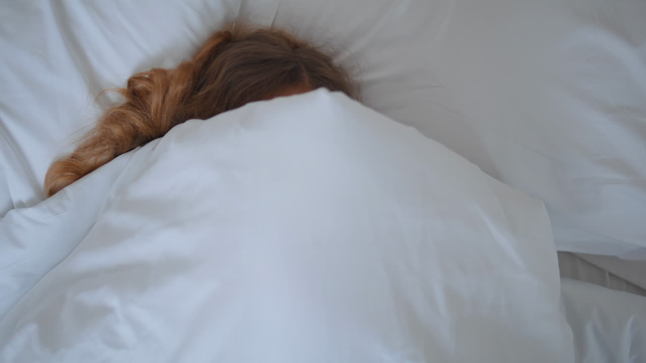 Child face covering blanket at morning bedroom closeup. Little baby awaking bed