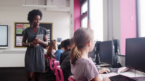 teacher helping female pupil in line of high school students working at screens in computer class