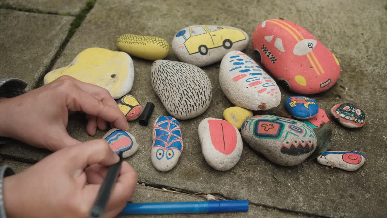 manos femeninas dibujando formas coloridas en piedras con marcadores