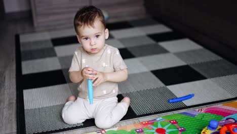 caucasian baby focused on the camera. kid sits on the floor holding and turning the toy in his hands.