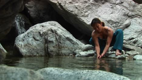 medium shot of a woman rockclimber washing her hands in a mountain pool