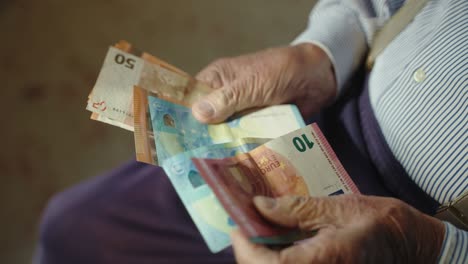 vista superior de un jubilado masculino contando ahorros de dinero, manos arrugadas de un abuelo anciano sosteniendo una pila de billetes de 10, 20 y 50 euros, papel moneda en manos de una persona anciana en jubilación