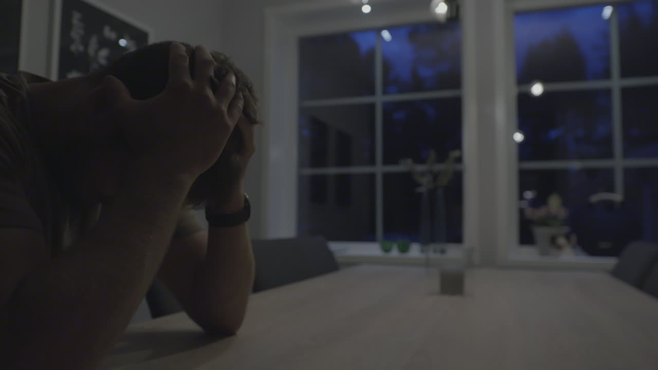 Sad Desperate Young Man sobbing and hiding face in his hands At Home late at night