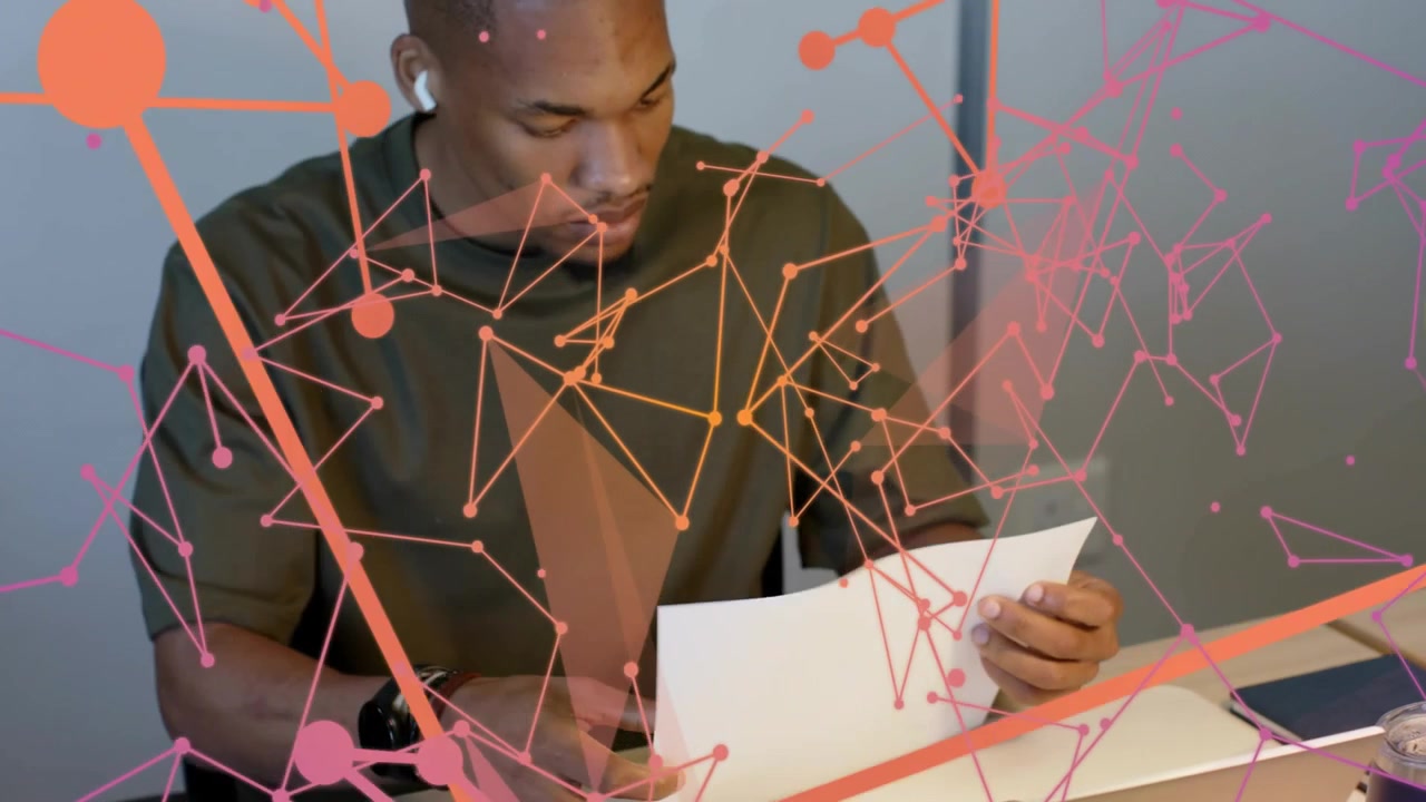 Man writing notes at desk, tapping laptop and flipping charts for design review, overlay aligning