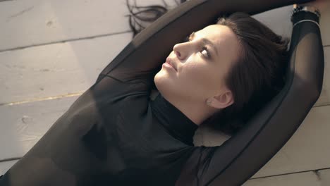 morena de cabello largo con maquillaje ligero yace en el suelo de madera