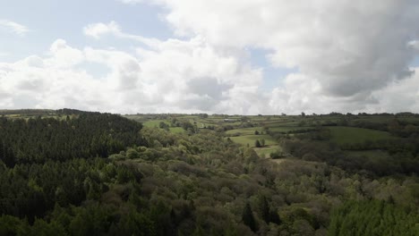 Luftaufnahmen-Von-Drohnen-Fliegen-über-Dichte-Grüne-Wälder-Und-Sanfte-Hügel-Mit-Flauschigen,-Weißen-Wolken-Am-Himmel