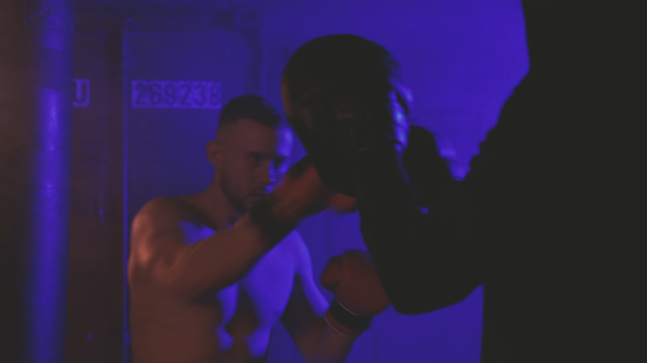 셔츠를 입지 않은 복서 남자가 스파링 장갑을 펀칭하여 워밍업