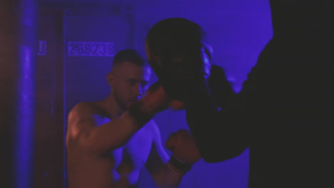 shirtless boxer man warms up by punching the sparring's gloves