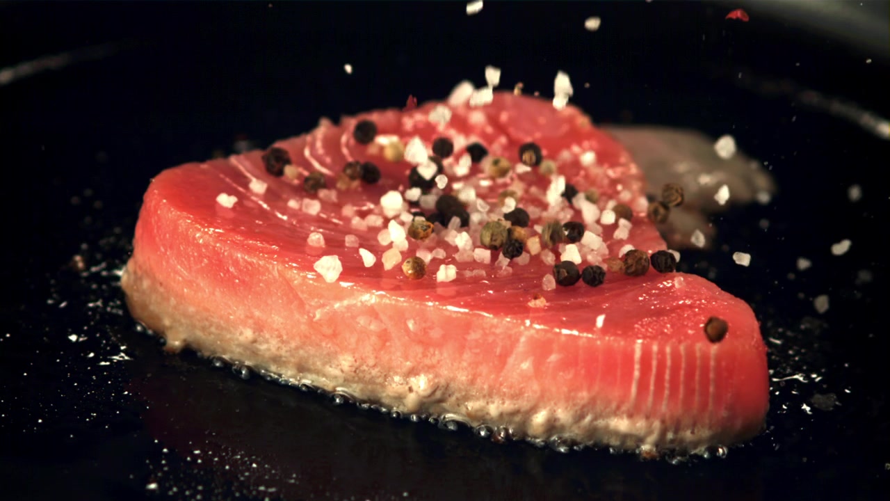 Slowmotion-optagelse af salt og peber, der falder ned på en rå tunbøf