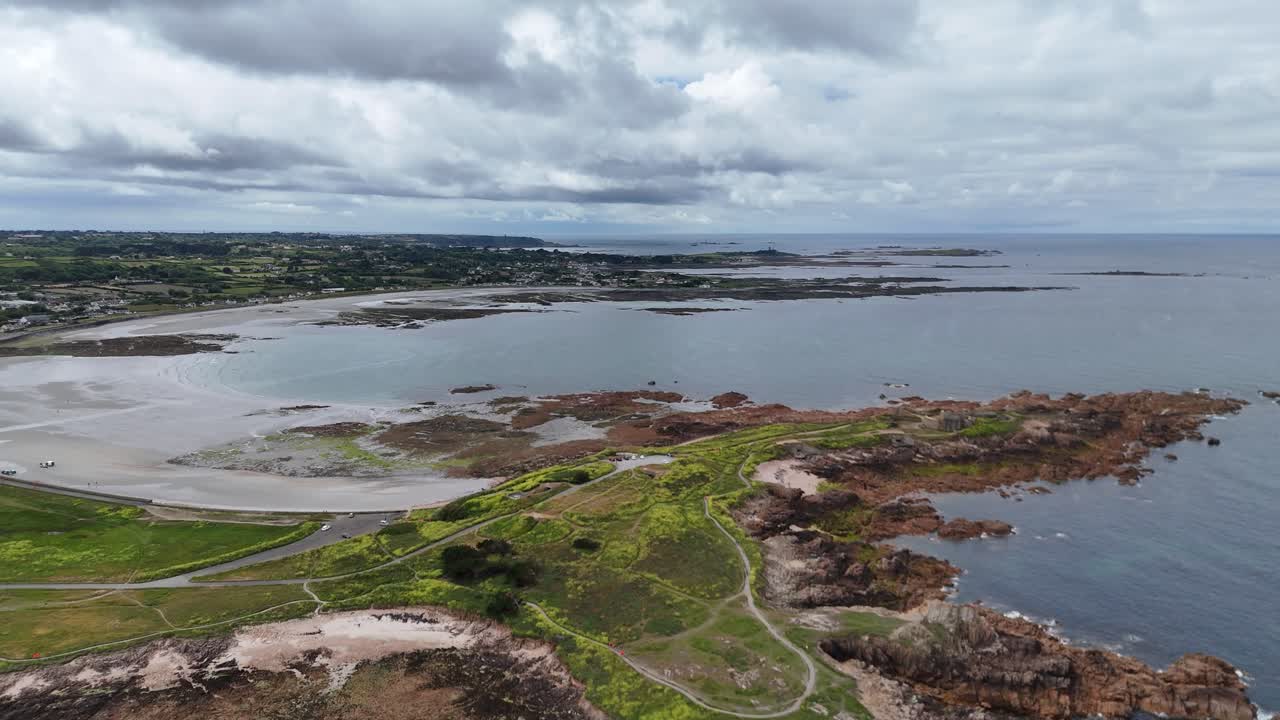 Guernsey west coast,slow flight over headland,bay and beach at low tide with interesting cloudy sky on bright calm day