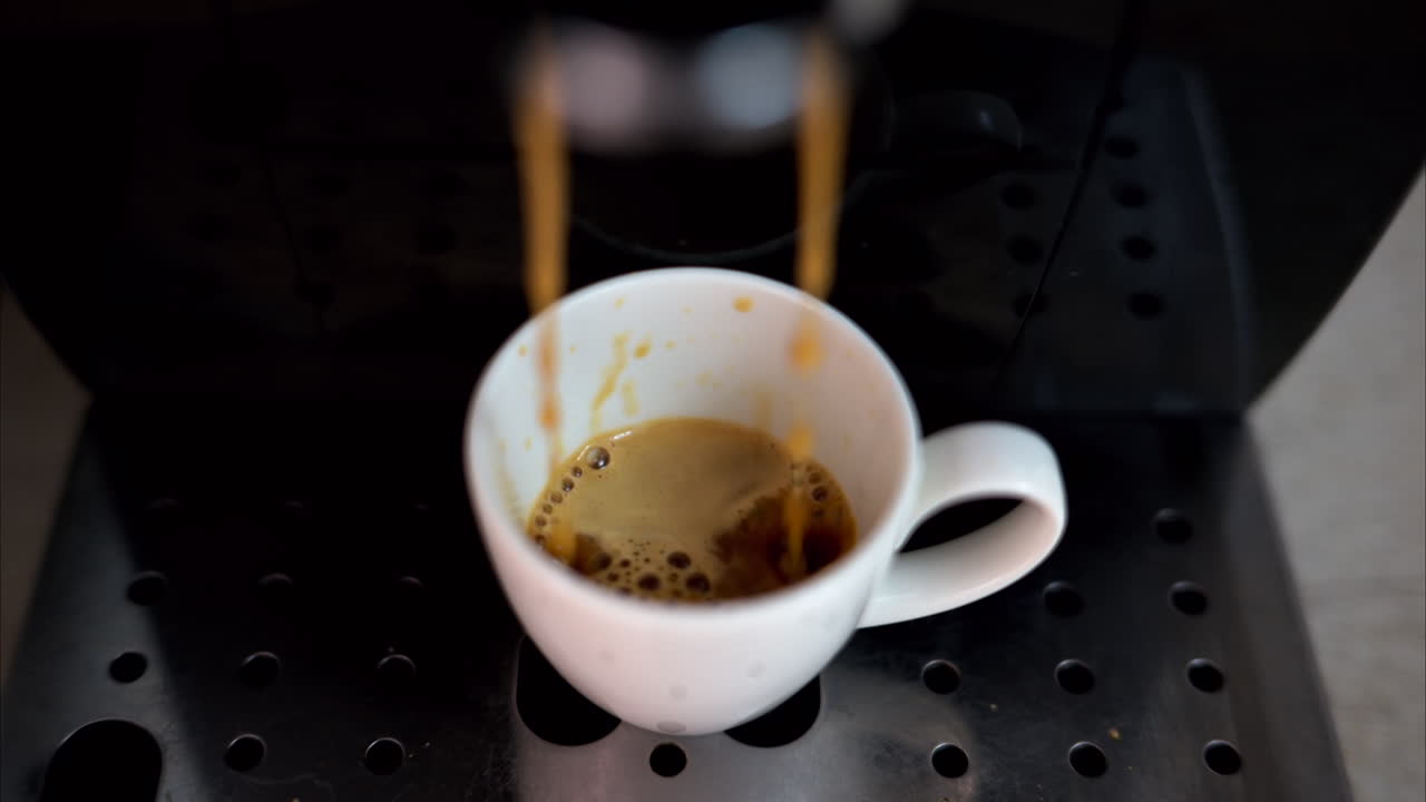 Coffee machine pouring arabica into a white espresso cup, slow motion, vertical screen