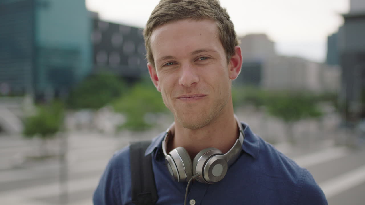 close up portrait of happy young caucasian man student looking at camera laughing cheerful on college campus in city background slow motion