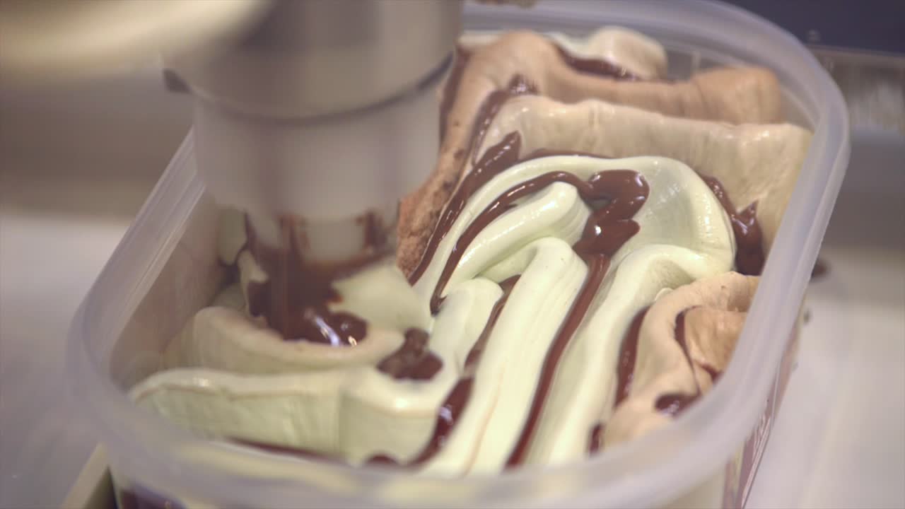 Primo piano di un braccio meccanico che riempie il gelato appena fatto con un motivo in un contenitore squround