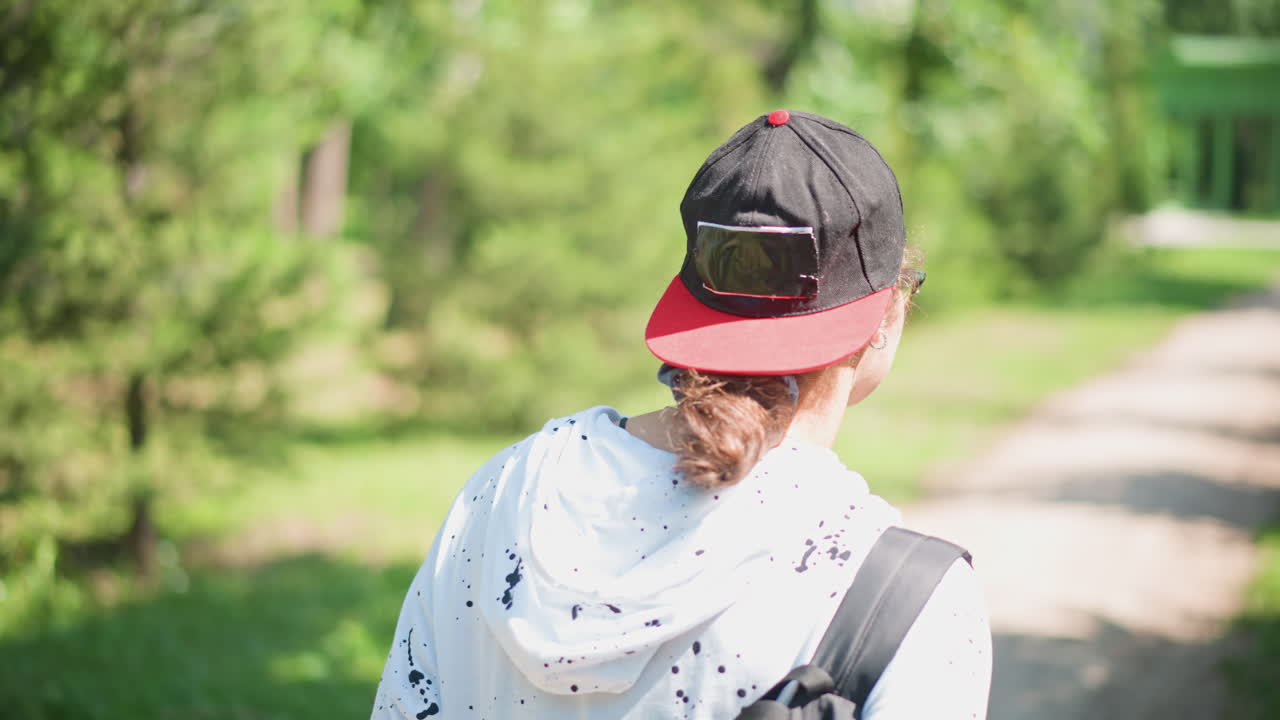 어깨에 백팩을 메고 모자를 거꾸로 쓴 채 숲길을 걷는 뒷모습, 꾸준한 발걸음과 탐험 분위기, 통근자에서 등산객으로, 흙길에 비치는 얼룩덜룩한 햇빛, 그늘진 나무