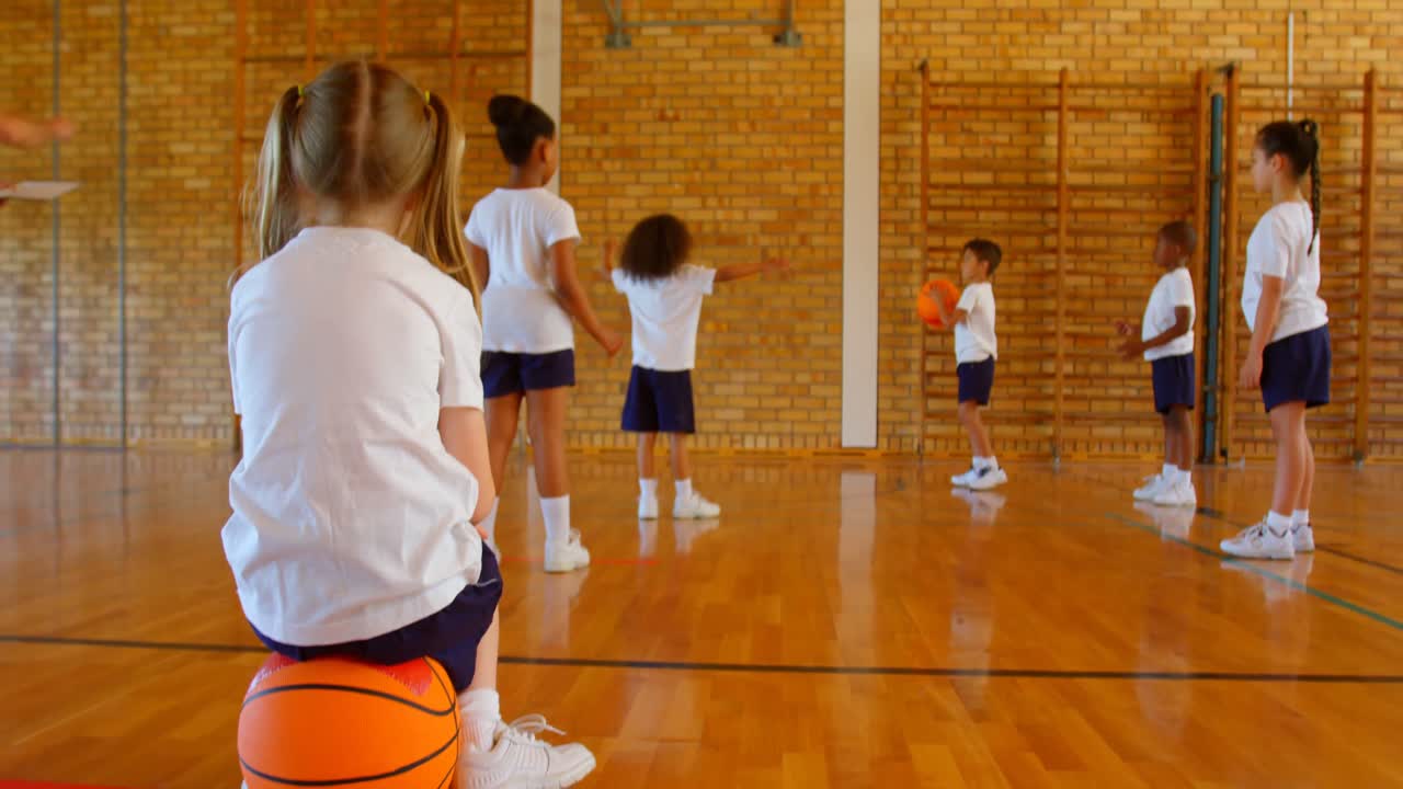 Scolaretta seduta su una palla da basket nel campo da basket a scuola 4K