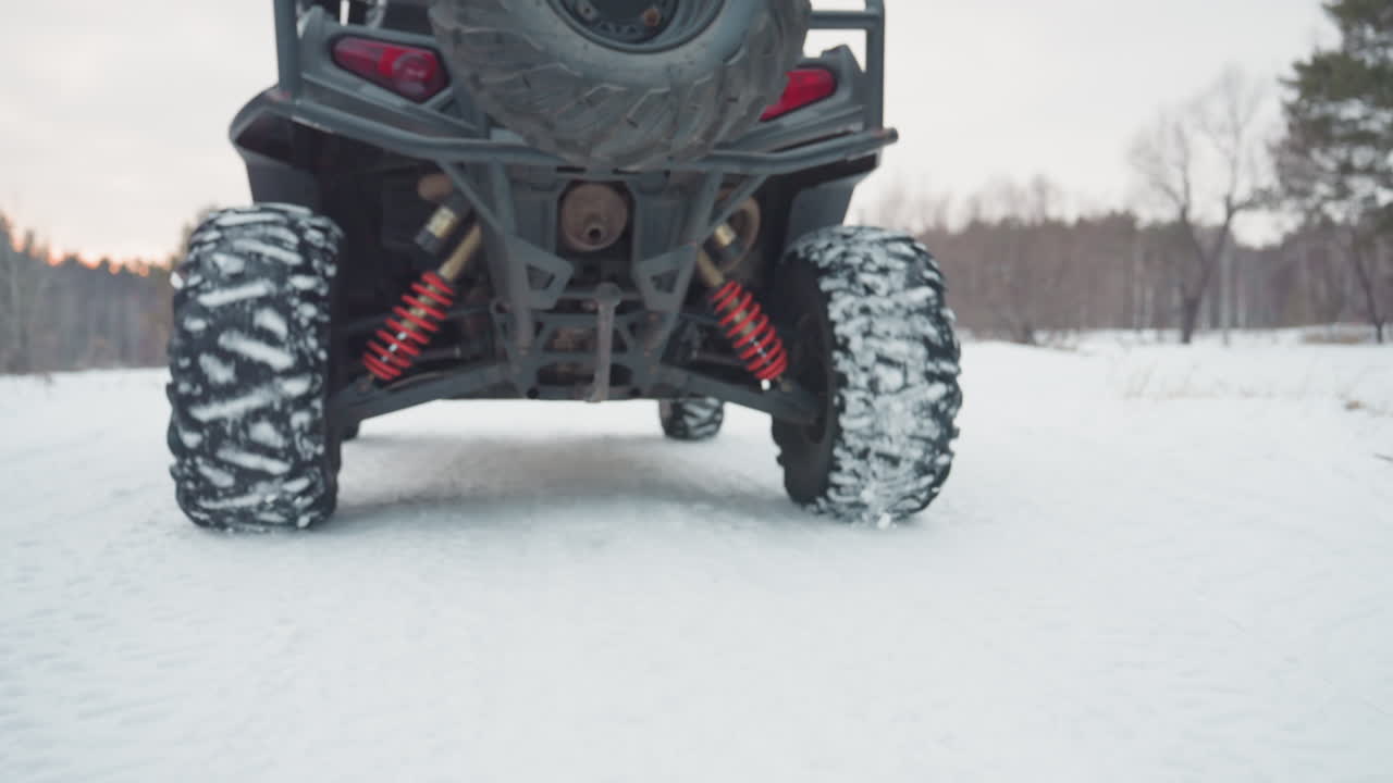 Ruota di scorta e ammortizzatori su un sentiero innevato. Veicolo fuoristrada robusto che attraversa la neve con un convoglio sullo sfondo. Sottoscocca di un camion con ruota di scorta e ammortizzatori tra terreno innevato e convoglio.