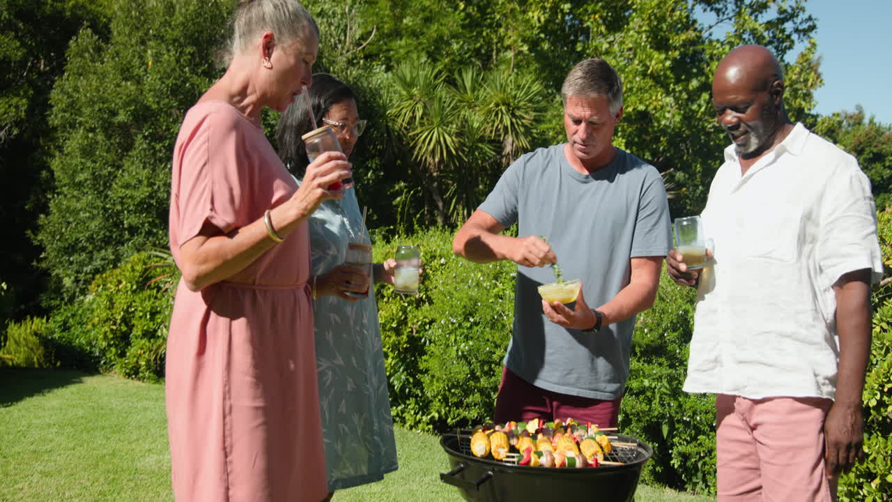 Diverse seniors enjoying in garden barbecue, grilling vegetables and toasting with drinks