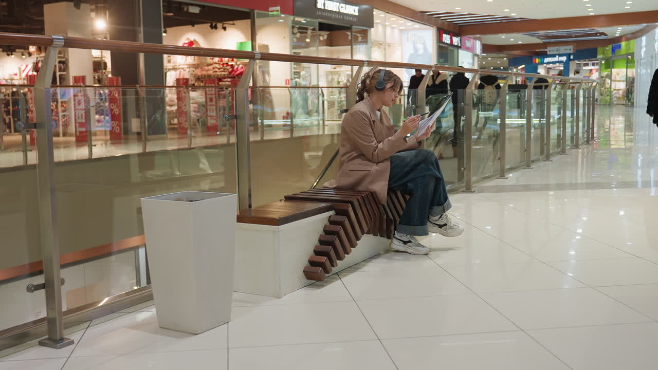 여성이 잡지를 보고 있어요. 세련된 여성이 손에 잡지를 들고 쇼핑몰 분위기를 즐기고 있네요. 편안한 여성 쇼핑객이 소매점 환경의 빛과 주변 조명 속에서 윤기 있는 잡지를 정독하고 있어요.