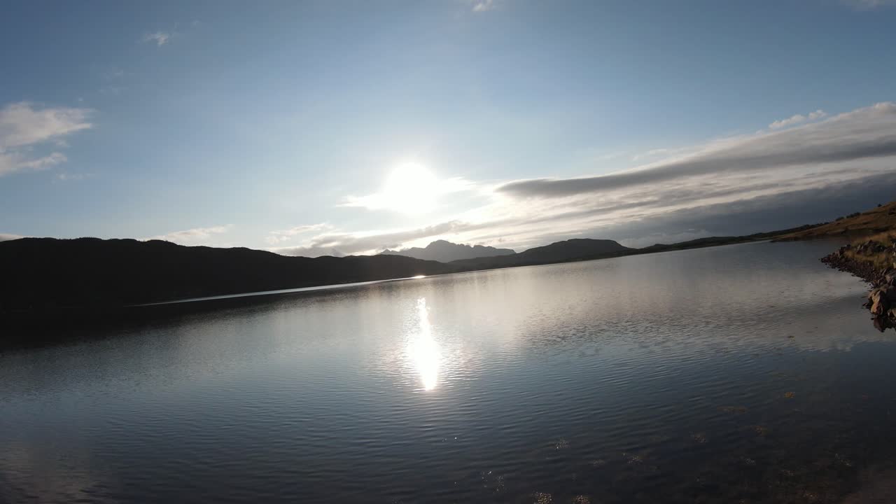 호수 옆에 있는 작은 풀밭 길을 따라 날고, 물에 반사된 태양을 향해 호수 위로 날아간 다음 배경에 산이 보이는 길을 향해 돌아갑니다.