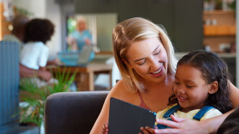 Mutter-Und-Tochter-Nutzen-Zu-Hause-Ein-Digitales-Tablet,-Im-Hintergrund-Eine-Familie-Mit-Mehreren-Generationen