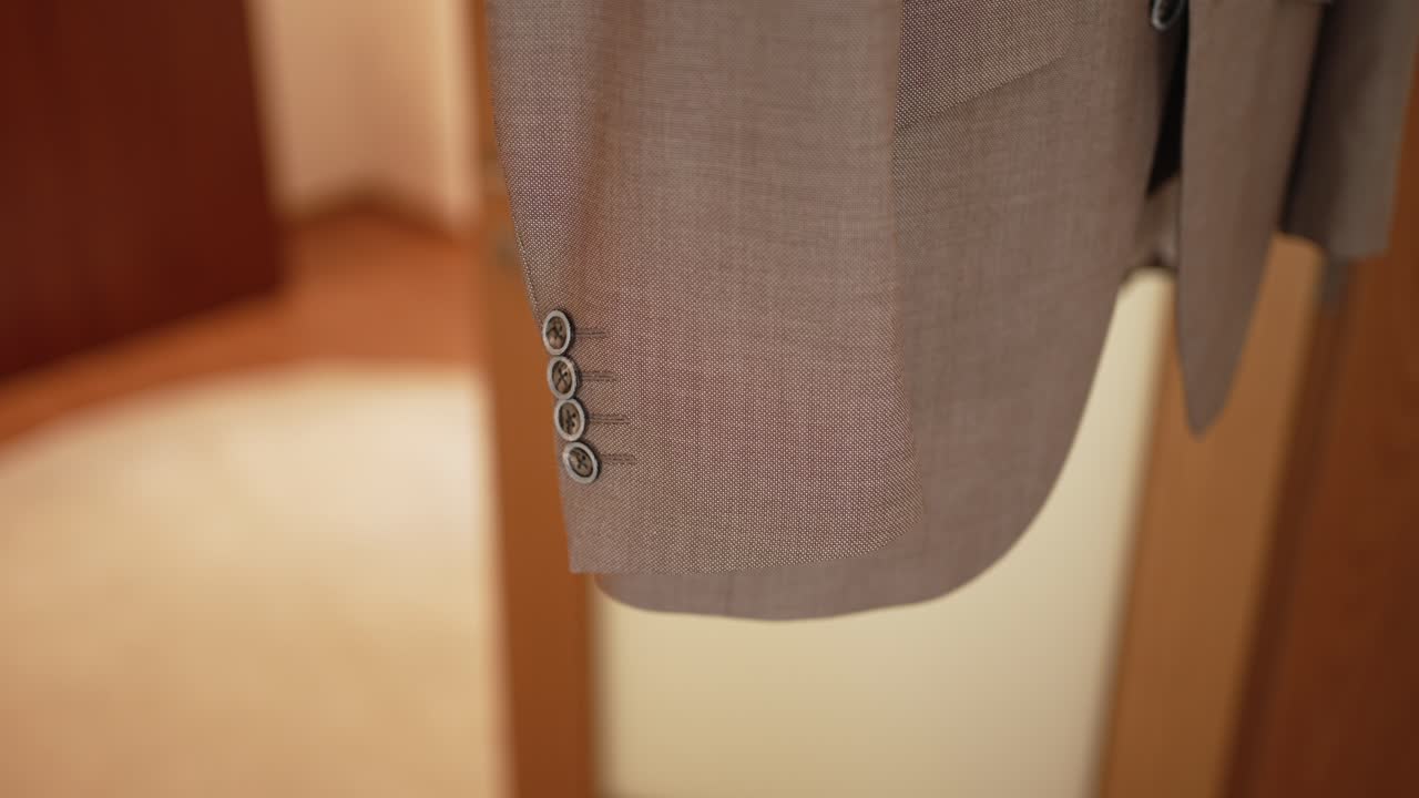close up of beige groom suit sleeve with buttons hanging in softly lit wedding room