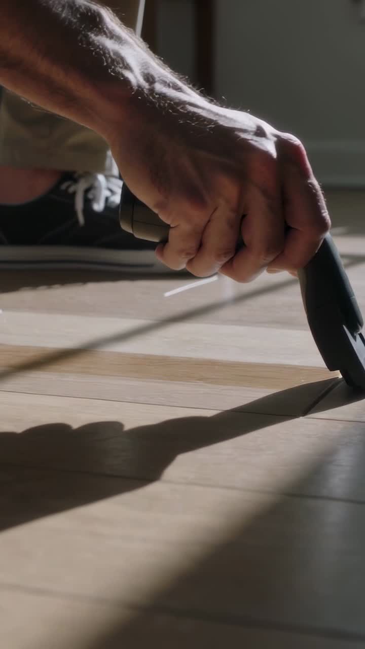 Vertical video: Placing blade on seam, man pulling knife on floor at home, lifting tape, sneaker