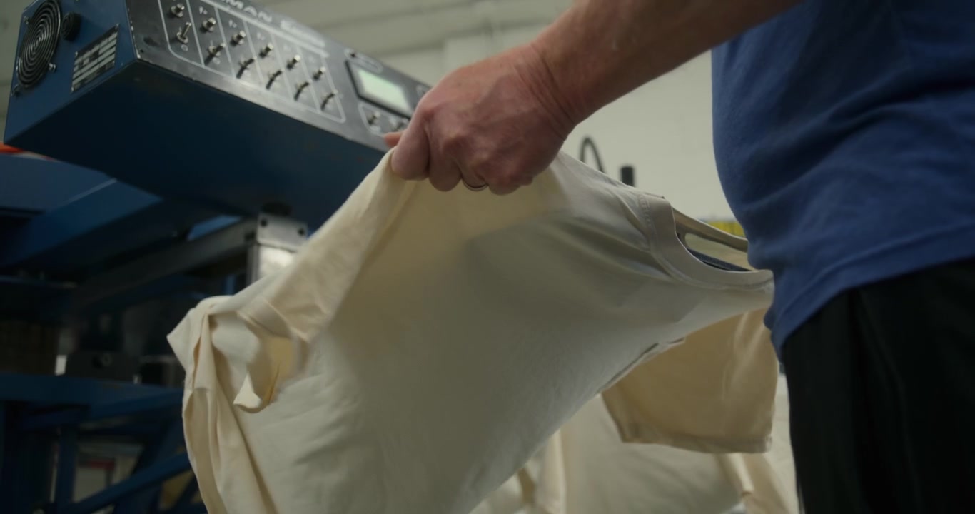Man Places T Shirt on Screen Printing Machine