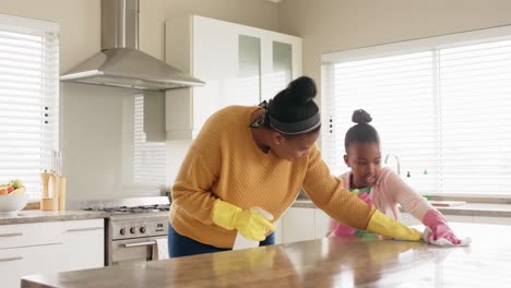 happy african american mother and daughter cleaning countertop in kitchen, in slow motion