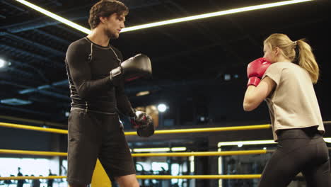 smiling coach training with female athlete on boxing ring. couple boxing at gym