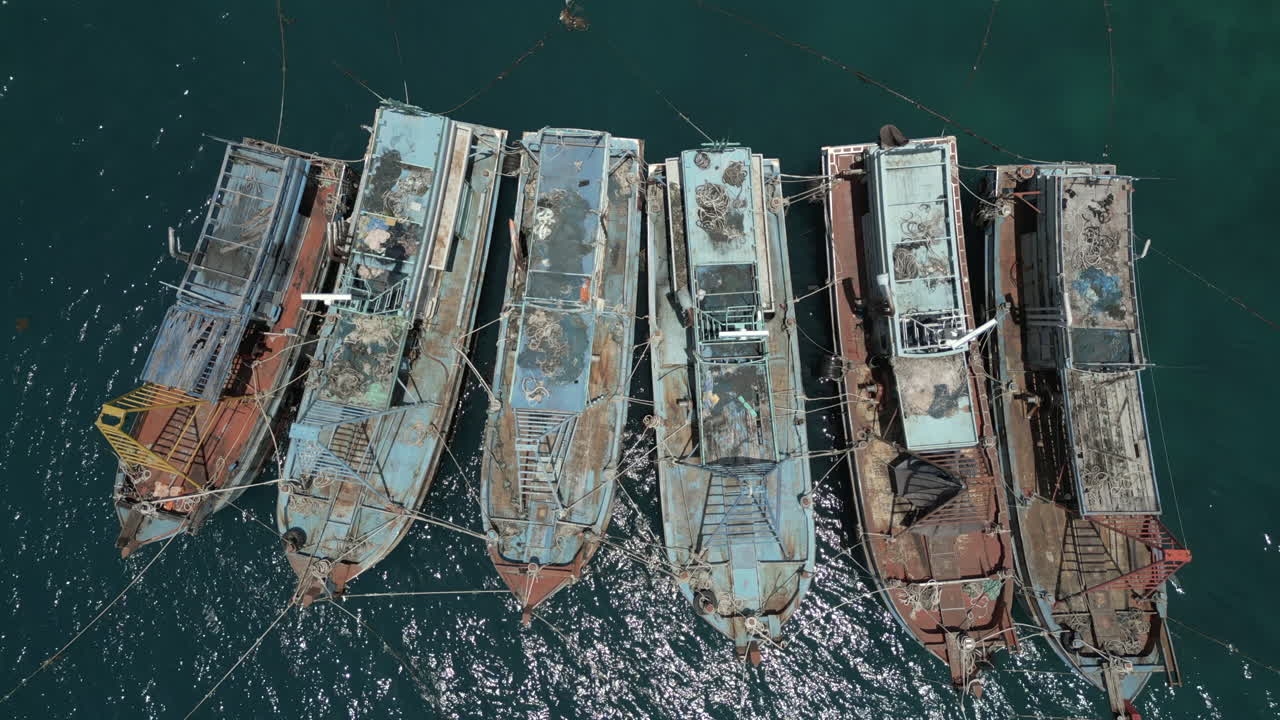 Una vista aérea cenital de un grupo de viejos barcos de pesca indonesios, dados de baja y atados entre sí. Los cascos de madera están desgastados y blanqueados por el sol bajo el calor tropical de Natuna.