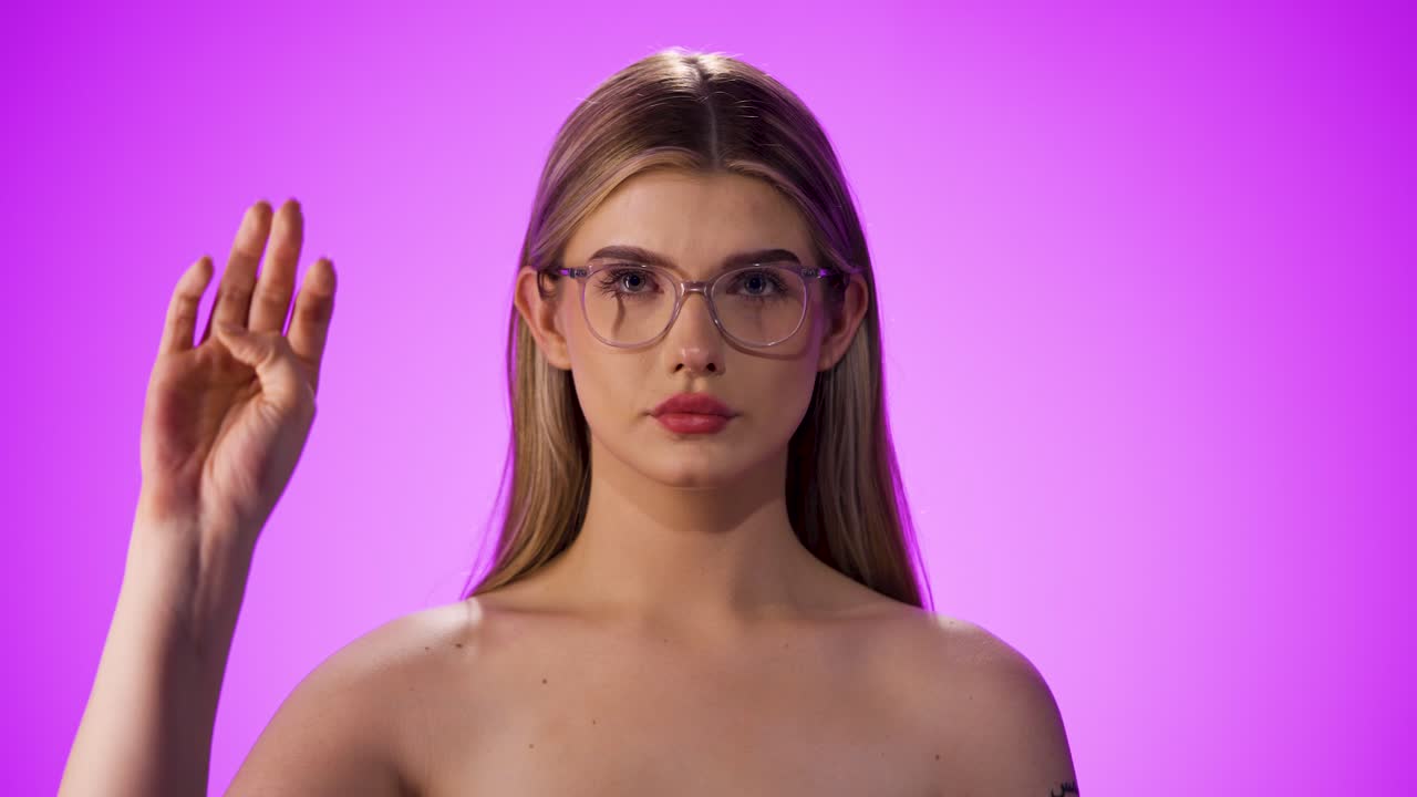 Medium shot of a young beautiful woman with a glasses while she makes a hand signal with her hand for a call for help because she needs help and is in danger