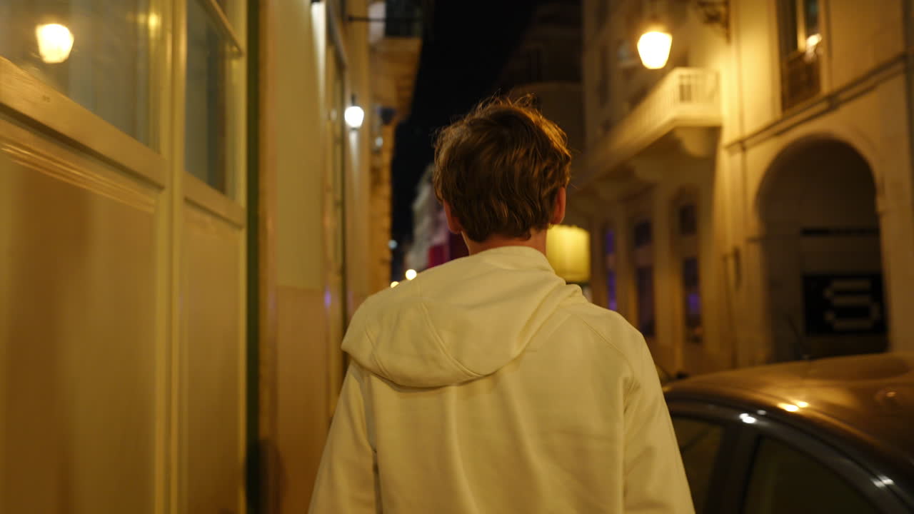 Solitary teen traveler wandering through historic European city streets, experiencing vibrant nightlife and illuminated architectural beauty during warm summer evening