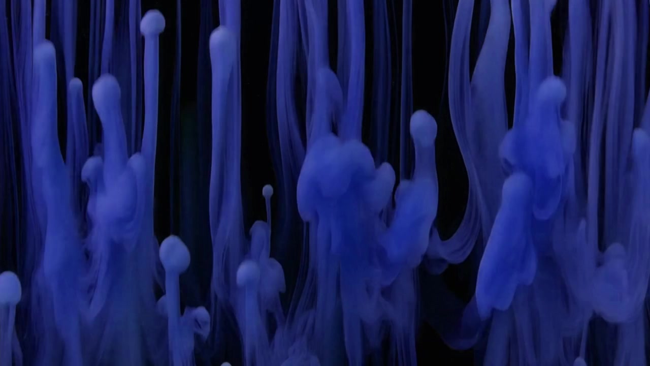 Gouttelettes d'encre bleue s'élevant dans l'eau sur fond noir
