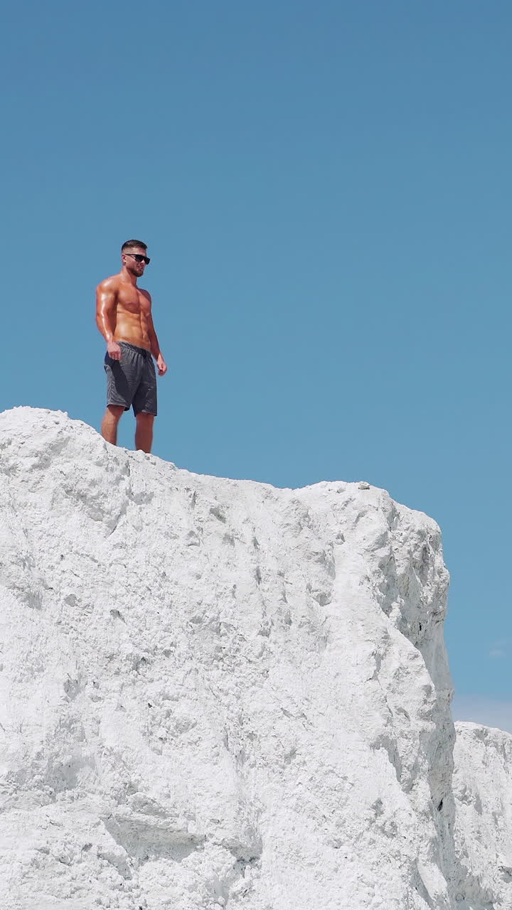 The winner man runs to the top of the mountain. A shirtless bodybuilder stands on a mountain against a blue sky. Vertical video