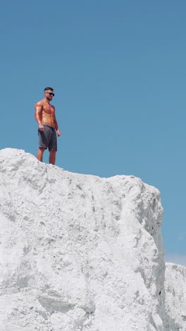 the winner man runs to the top of the mountain. a shirtless bodybuilder stands on a mountain against a blue sky. vertical video