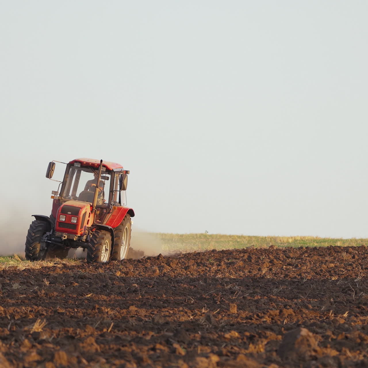 Tractor plowing fields, preparing land for sowing. Farmer in tractor preparing land in farmlands outdoors. Agricultural industry.