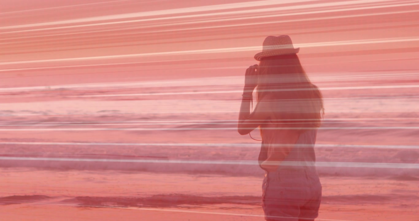 Female photographer brimmed-hat raising camera capturing horizon while waves rolling pink overlay