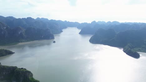 drone zooms in above tranquil blue bay with limestone formations and boats cruising below